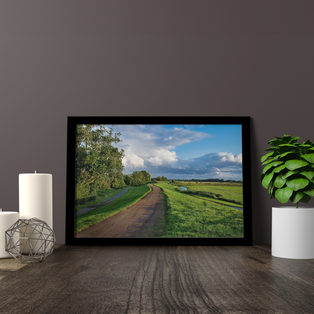 Foto de paisaje en metacrilato con marco negro sobre una superficie de madera, junto a velas y una planta