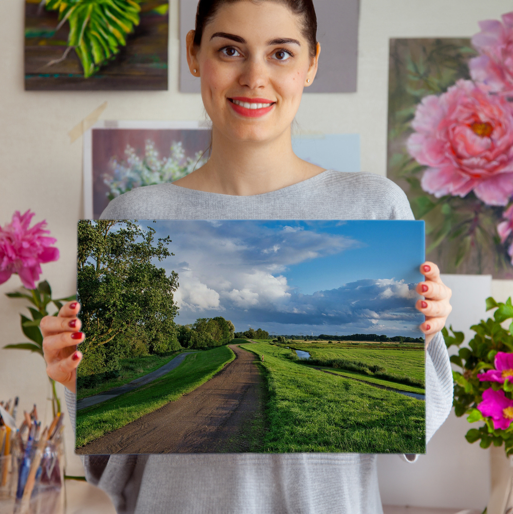 Foto en metacrilato sin marco con camino rural, prados y cielo con nubes, delante de cuadros florales