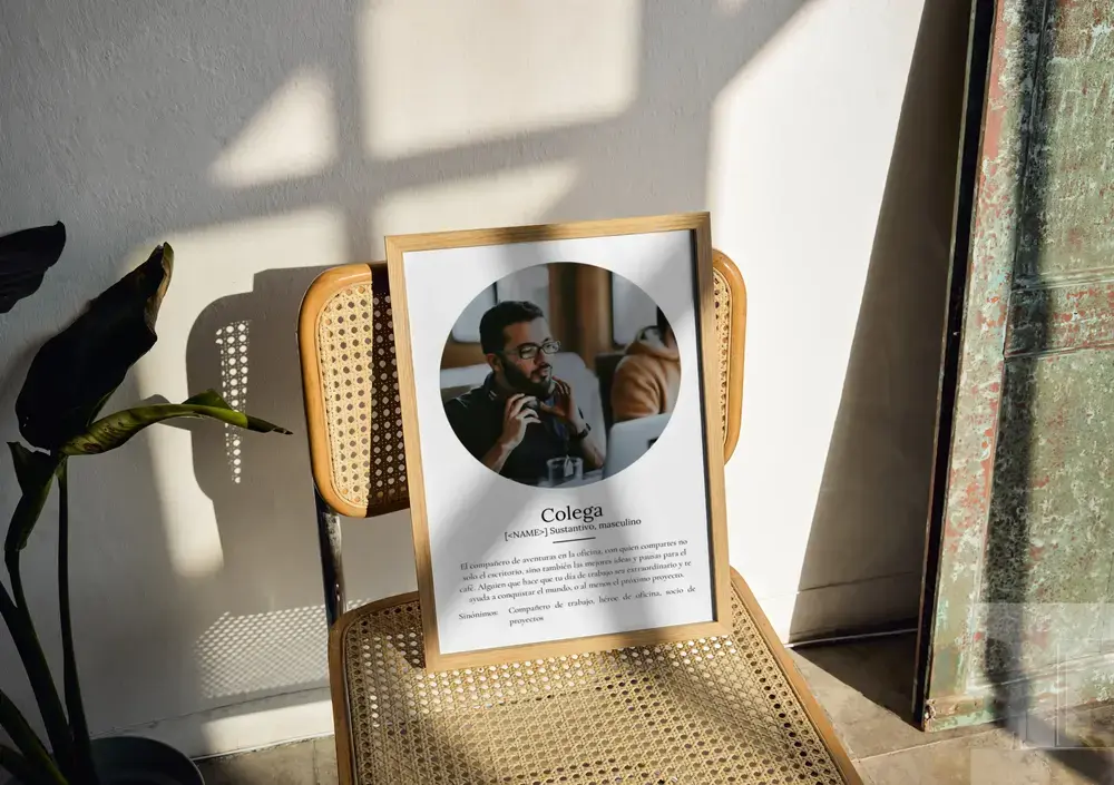 Póster estilo diccionario con foto circular y marco de madera, apoyado en una silla de rejilla junto a la ventana