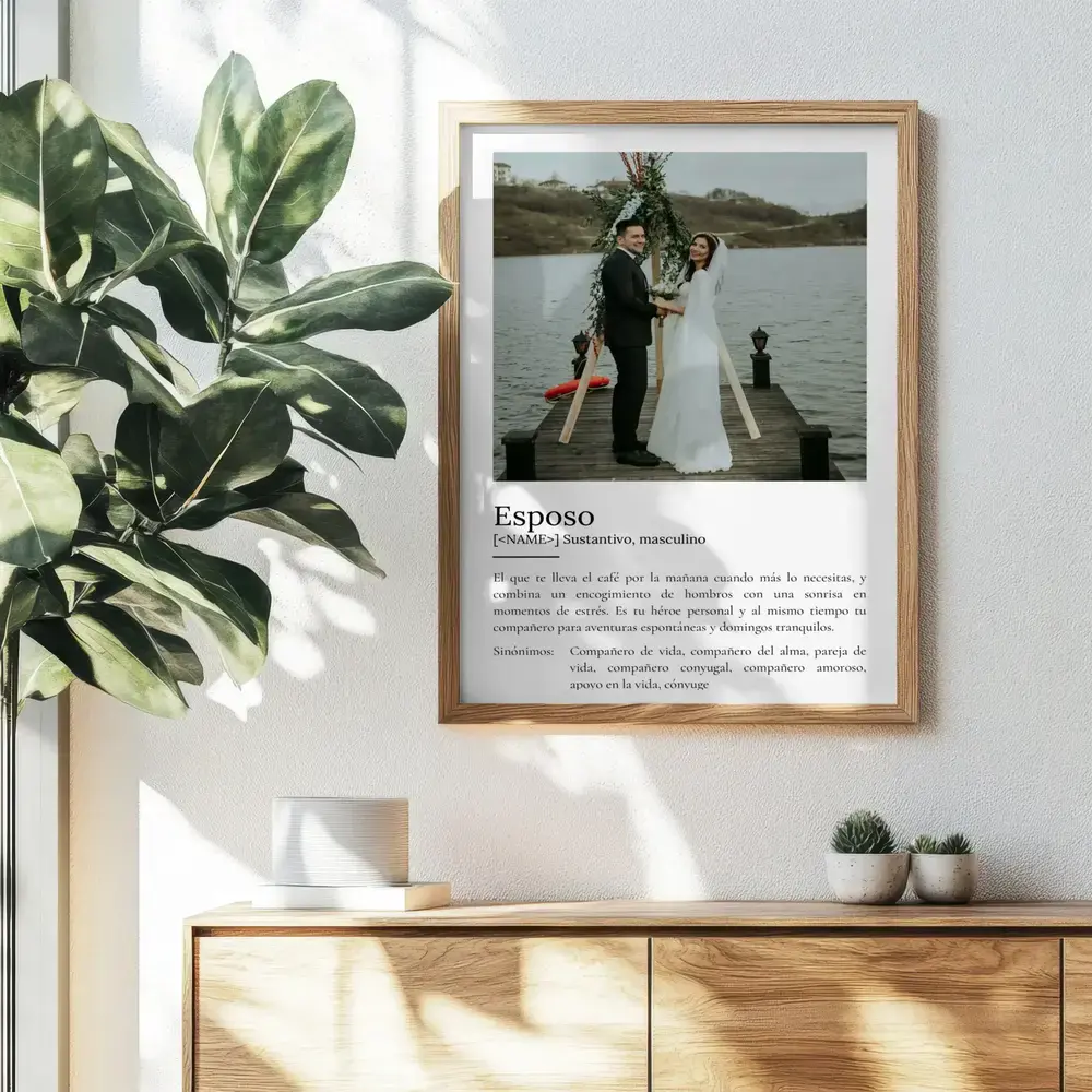 Lámina estilo diccionario con foto de boda en marco de madera, colgada sobre un aparador junto a una planta